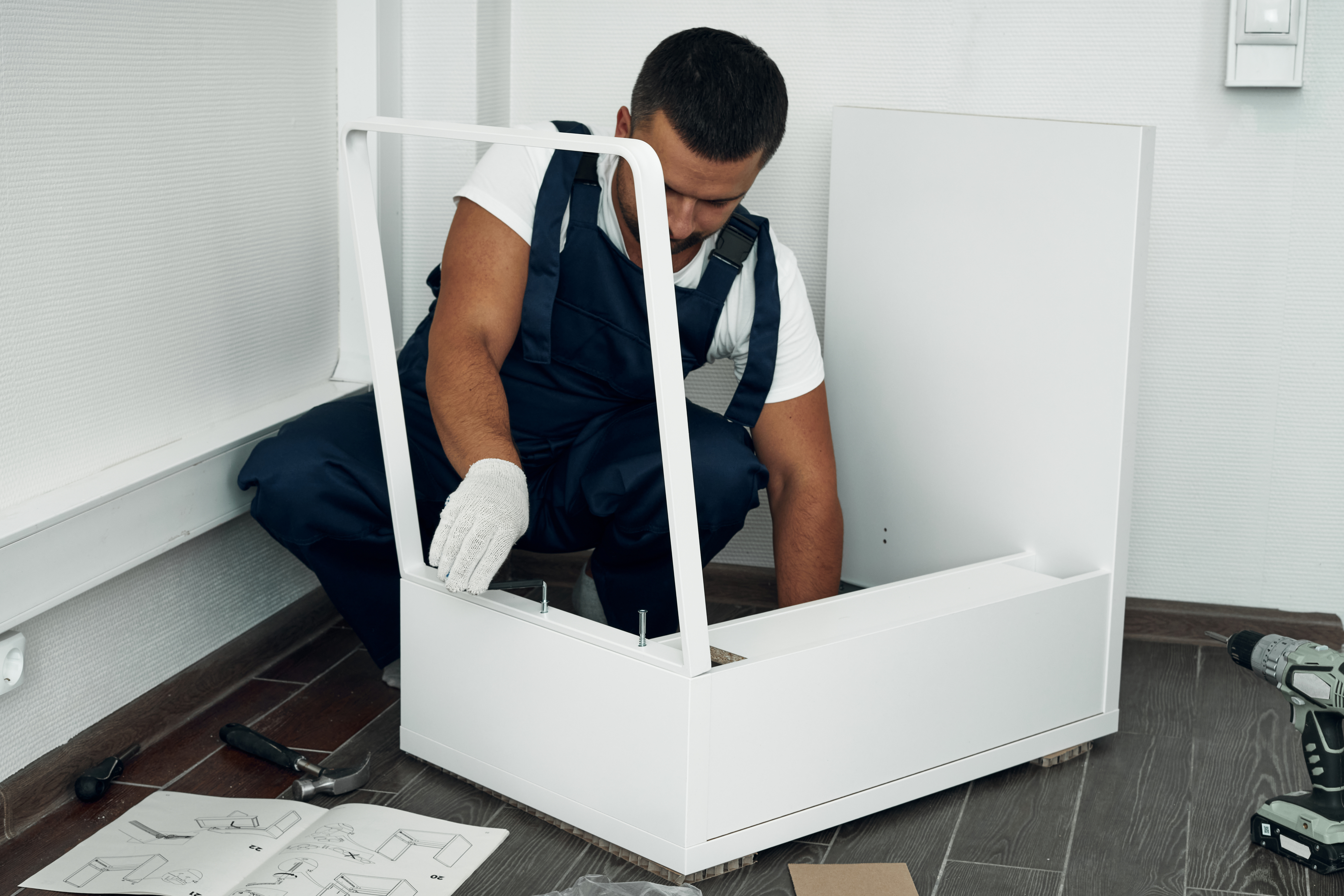 Ein Handwerker baut ein Möbelstück zusammen und arbeitet konzentriert mit Schrauben und Werkzeug. Neben ihm liegen Montageanleitung und weitere Arbeitsmaterialien bereit. Wir übernehmen Ihren Seniorenumzug in Hamburg und Umgebung.