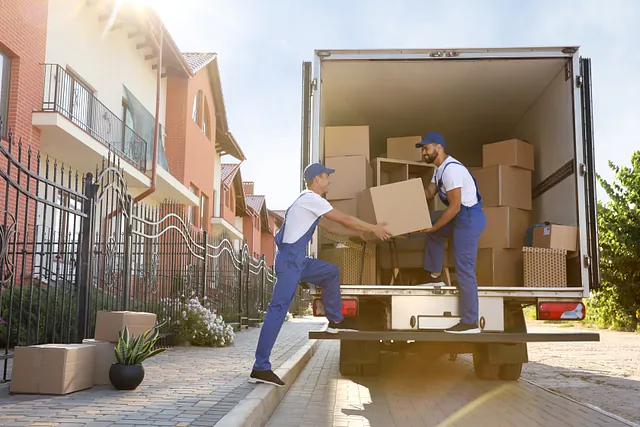 Zwei Umzugshelfer laden Kartons in einen Transporter vor einem Wohnhaus. Sie arbeiten im Team und tragen blaue Arbeitskleidung und Kappen. Wir führen Seniorenumzüge in Hamburg und Umgebung durch. 
